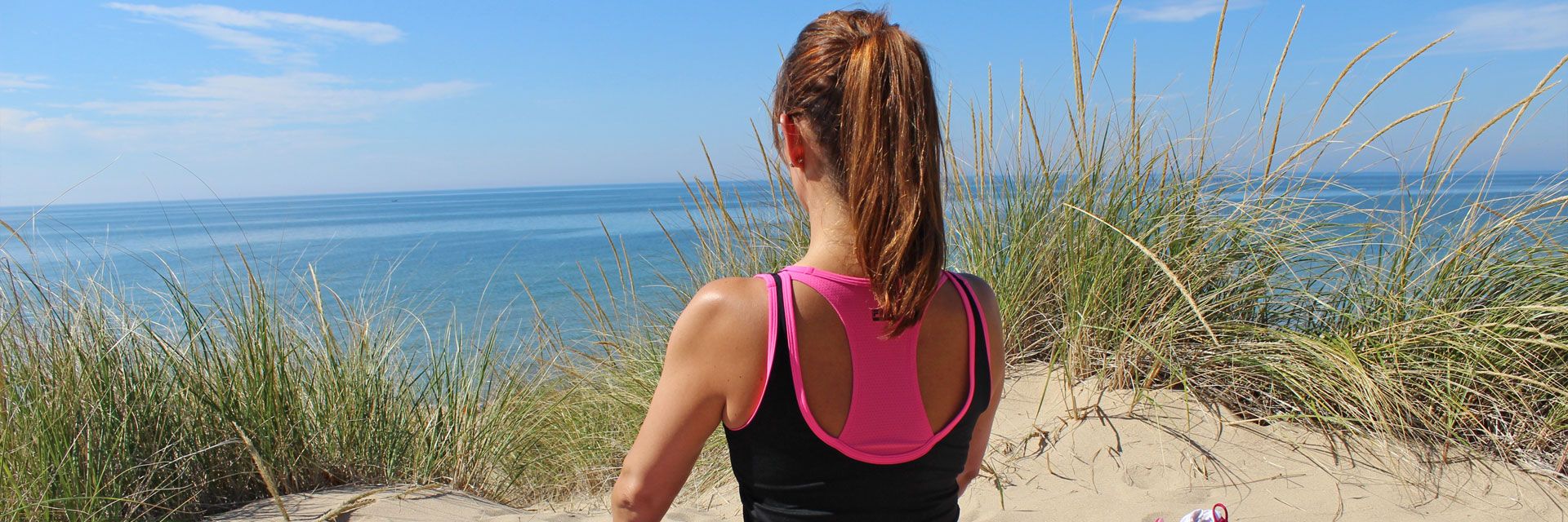 Foto: In einer Düne nahe des Meeres sitzt eine junge Frau gelassen auf ihrer Yogamatte. Sie kommt zur Ruhe ohne einzuschlafen.