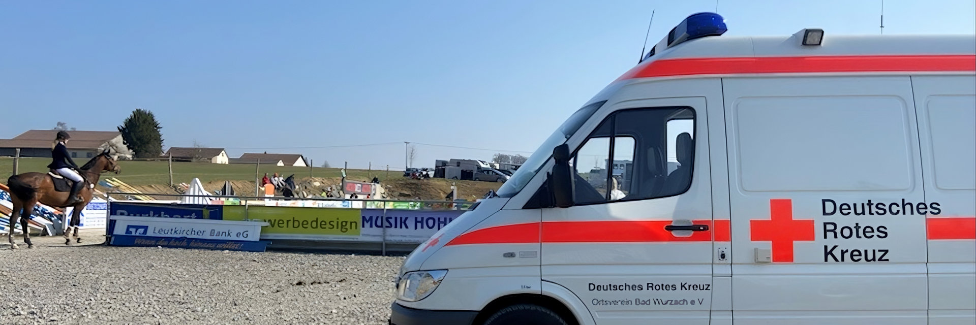 Foto: Mitarbeiter des DRK-Rettungsdienstes stehen vor einem Notarztwagen.
