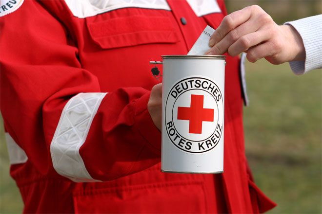 Foto: Eine junge Frau steckt einen Geldschein in eine Spendendose, die ein DRK-Helfer vor sich hält.